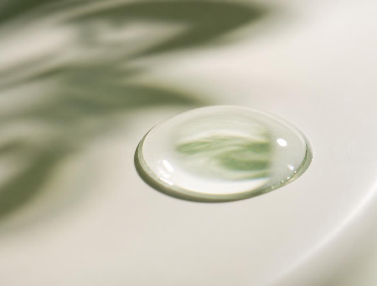 A single droplet of clear serum on a smooth ivory ceramic surface